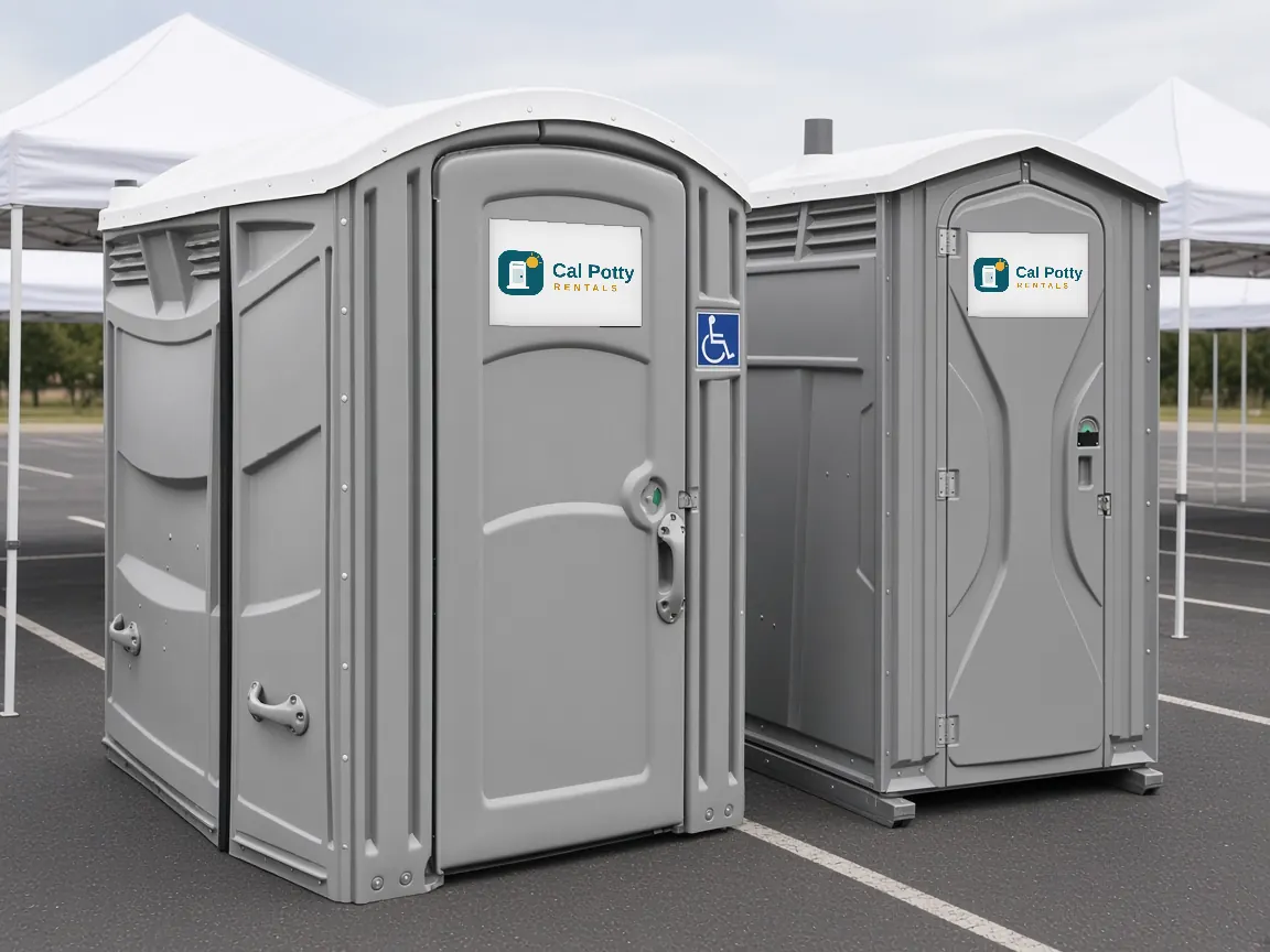 A grey ADA-accessible portable restroom with a wheelchair sign beside a standard grey unit in a parking area with white tents
